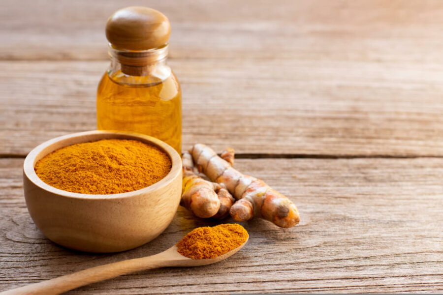 A bowl of turmeric powder, a wooden spoon with turmeric powder in and a bottle of turmeric oil