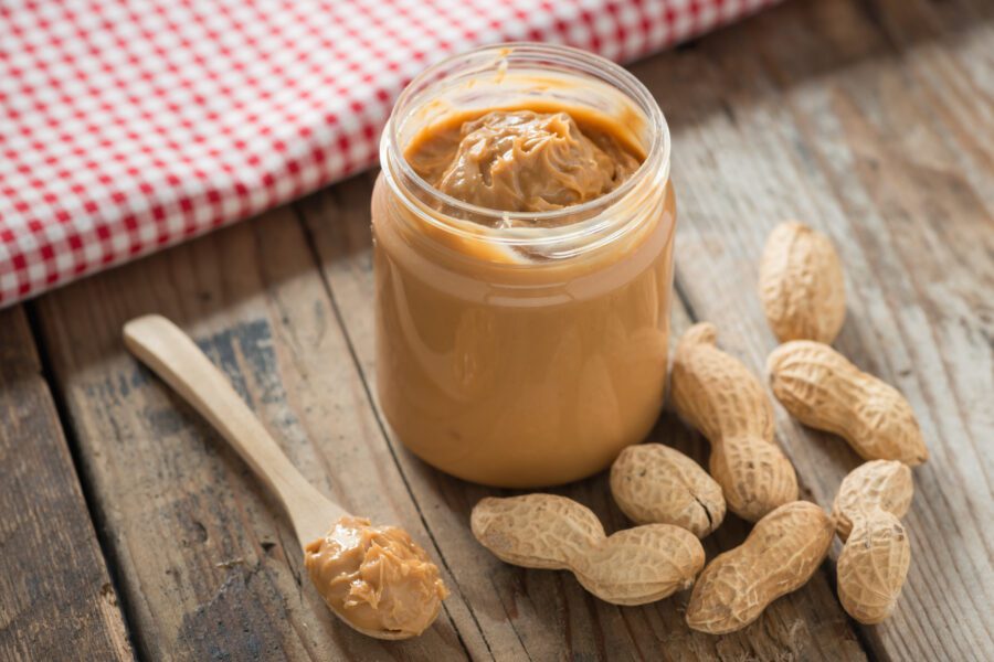 peanut butter in a jar with peanuts scattered around it