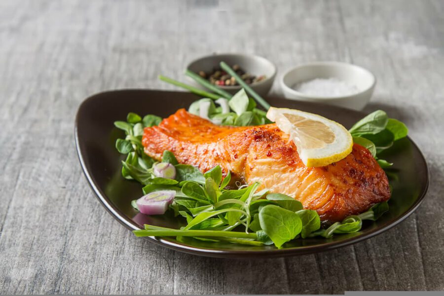 A bowl of green leafy salad with a grilled salmon on it