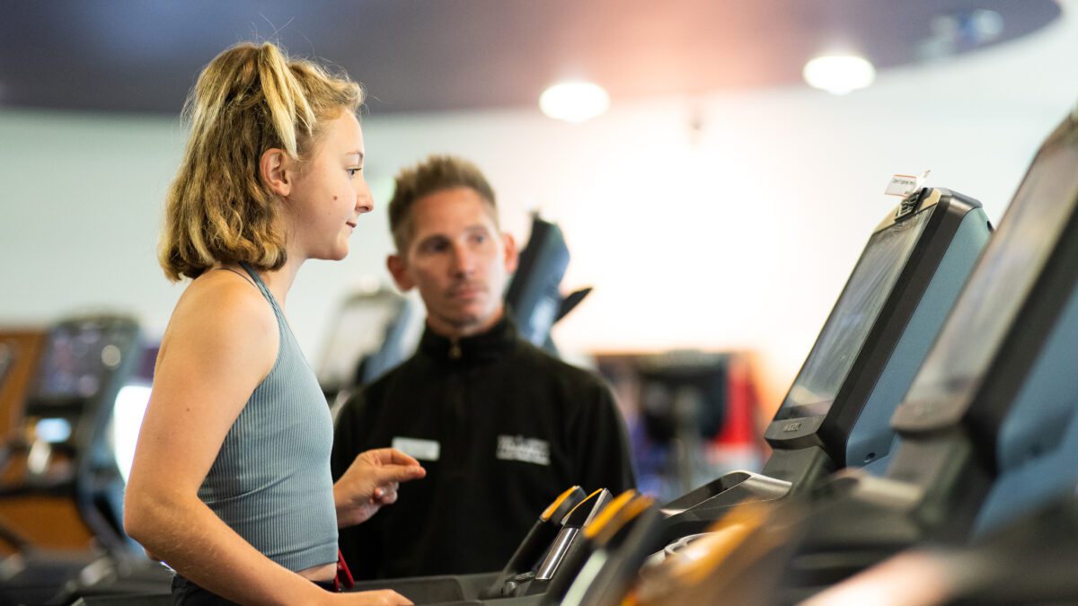 Personal trainer advising client on treadmill