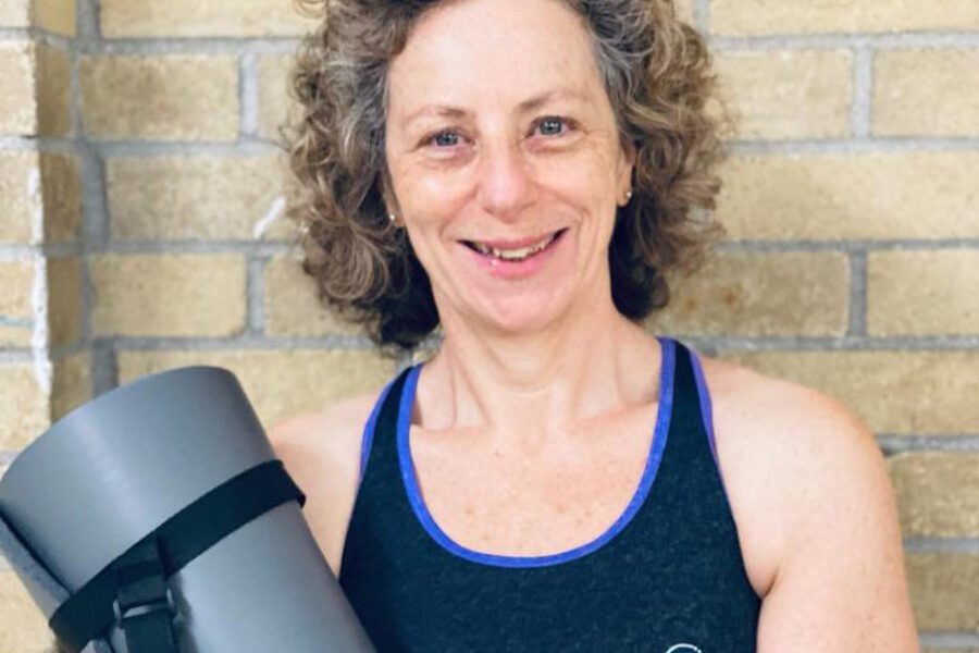 Karen Menis smiling, holding a yoga mat