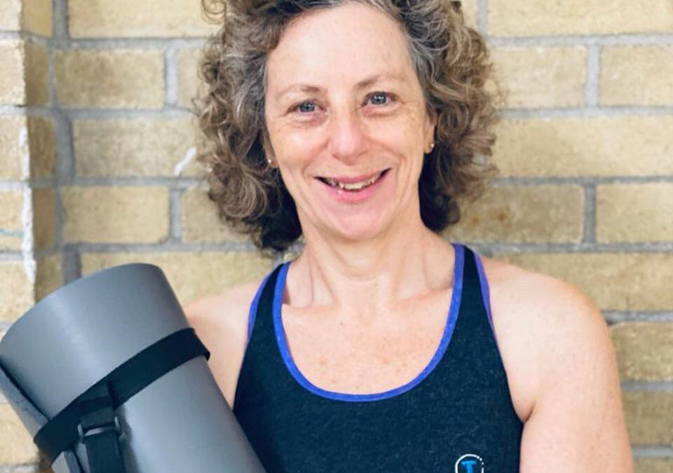 Karen Menis smiling, holding a yoga mat