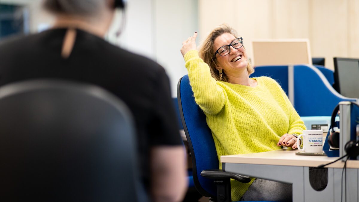 Woman seated at desk chair smiling at her coworker