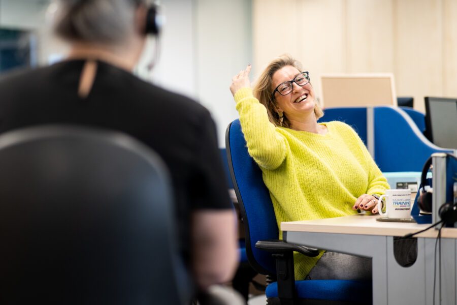 Woman seated at desk chair smiling at her coworker