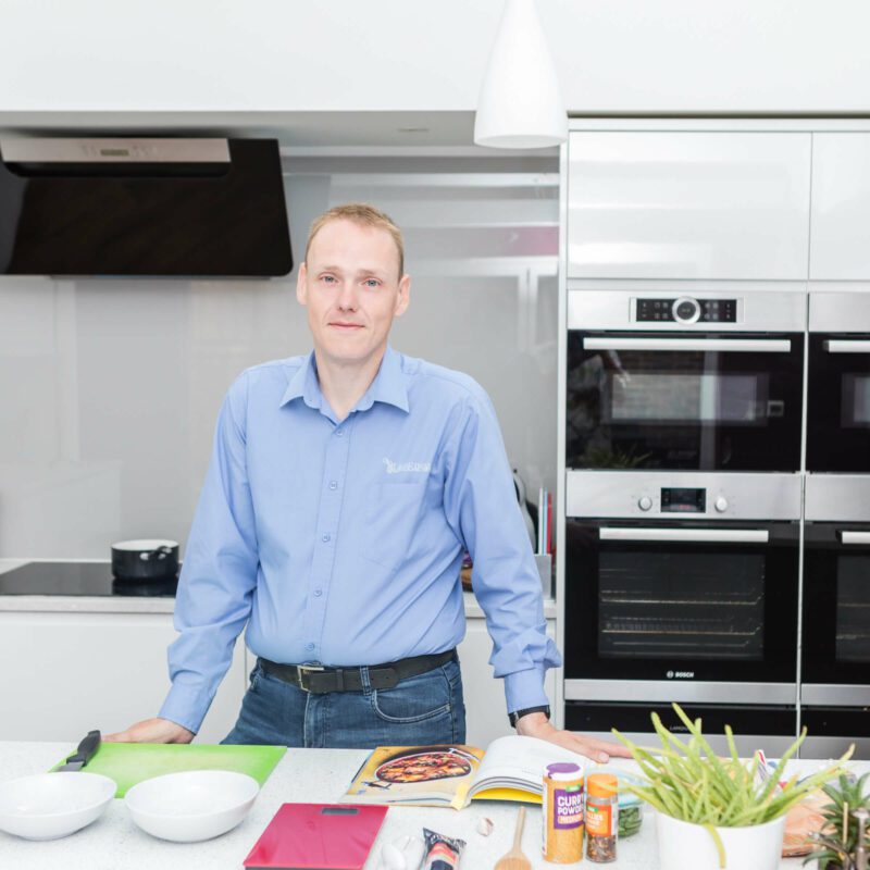 David standing in a blue shirt in a white kitchen with healthy ingredients on the table