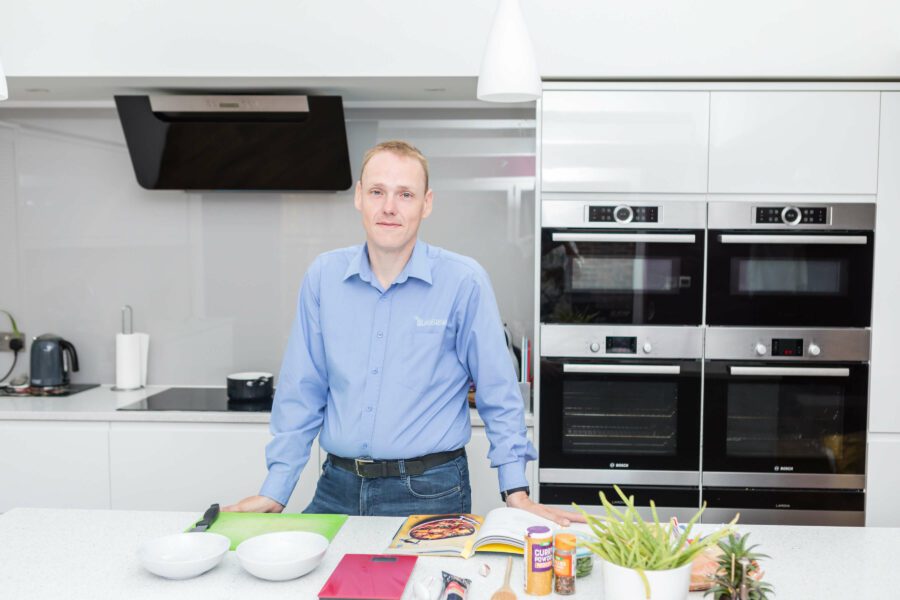 David standing in a blue shirt in a white kitchen with healthy ingredients on the table