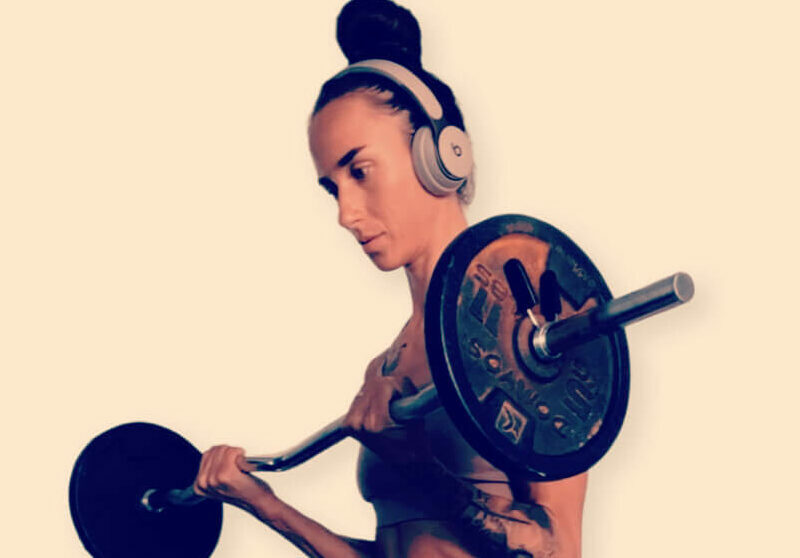 A slim woman holding a barbell listening to headphones.