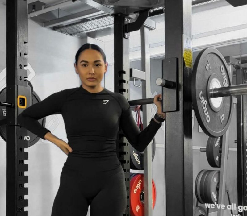 A woman standing in a squat rack holding a barbell
