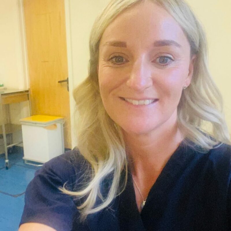 A young blonde woman in nurses scrubs smiling at the camera