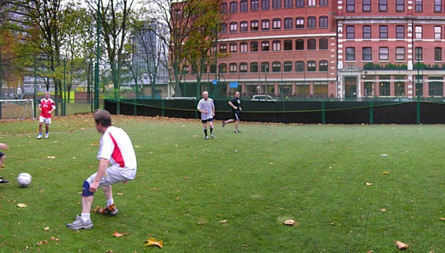 Men playing football on a pitch in inner city London.