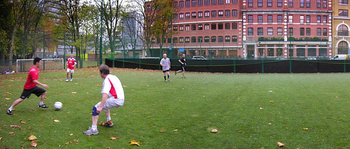 Men playing football on a pitch in inner city London.