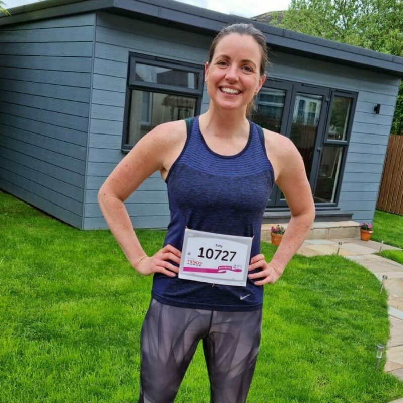 A woman standing in her garden in front of a shed wearing running clothes