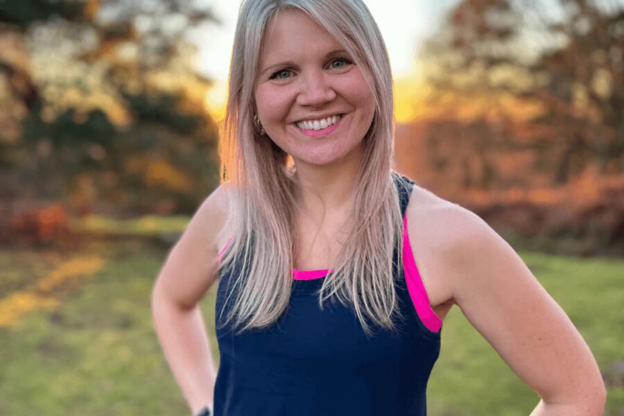 A woman standing in a garden with her hands on her hips looking into the camera wearing a gym vest