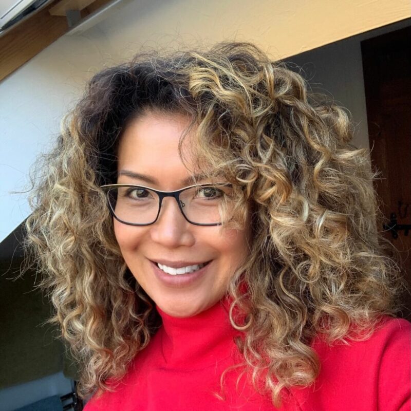 Woman with curly hair and glasses smiling at the camera