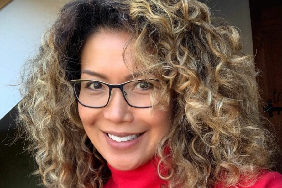 Woman with curly hair and glasses smiling at the camera