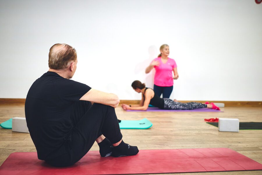 man sat on red pilates mat listening to instructor