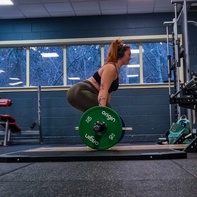 A woman lifting a heavy barbell facing sideways to the camera