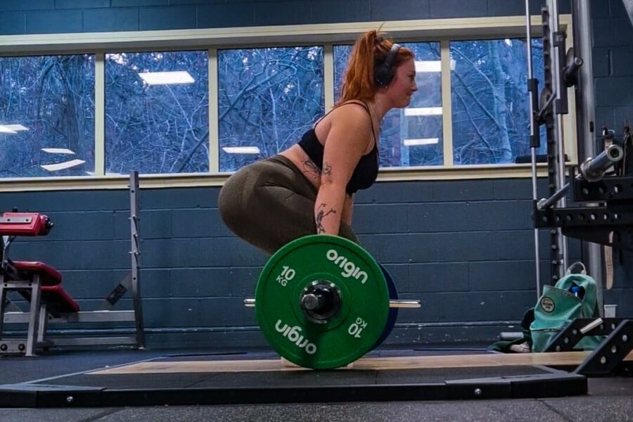 A woman lifting a heavy barbell facing sideways to the camera