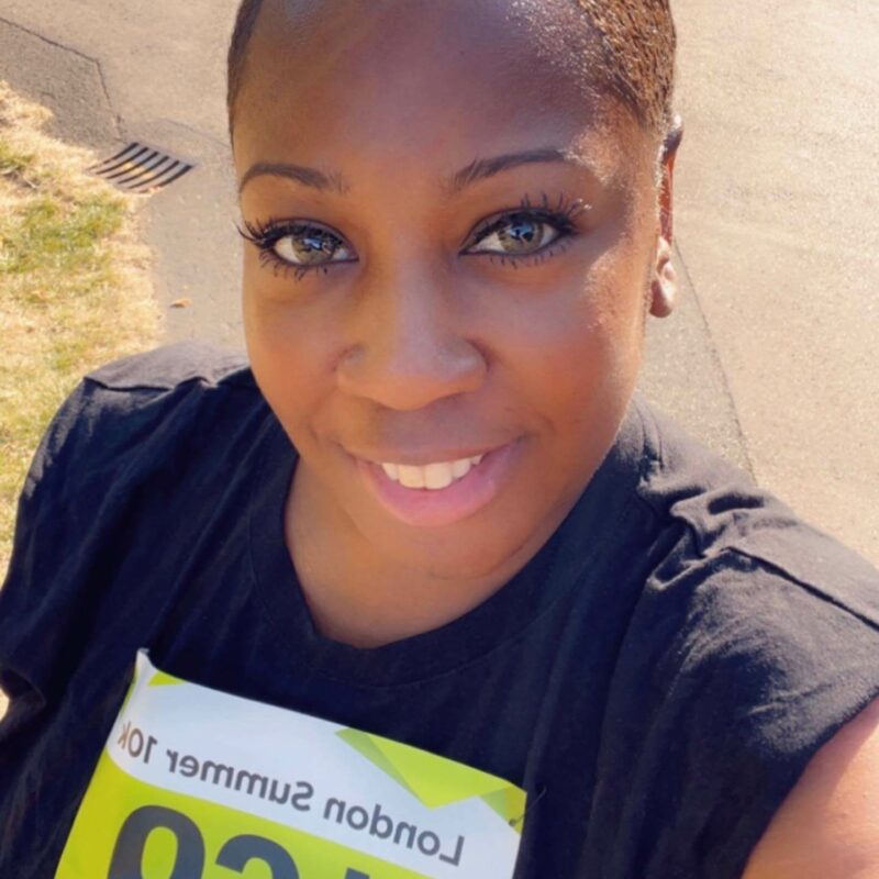 A woman close to the camera smiling, wearing a running number