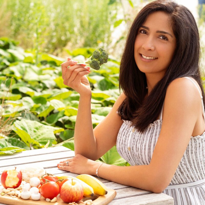 A woman with dark hair sitting at the table eating a broccoli