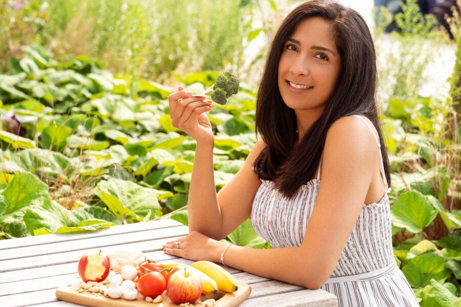 A woman with dark hair sitting at the table eating a broccoli