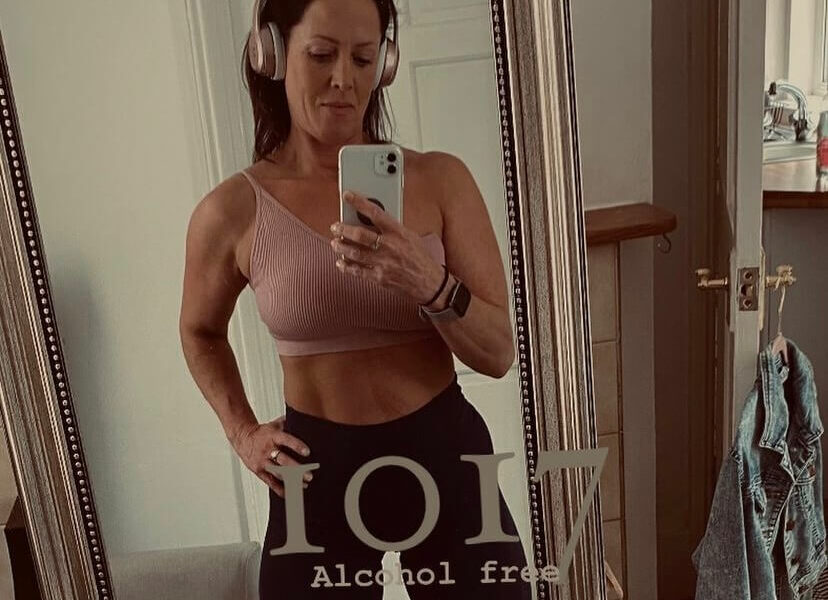 A woman standing in front of a mirror with writing over the front saying she has been "1017 alcohol free"