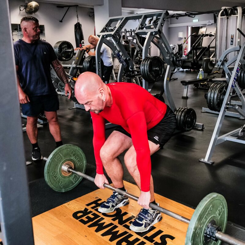 A man lifting a barbell from the floor wearing a red long sleeve shirt