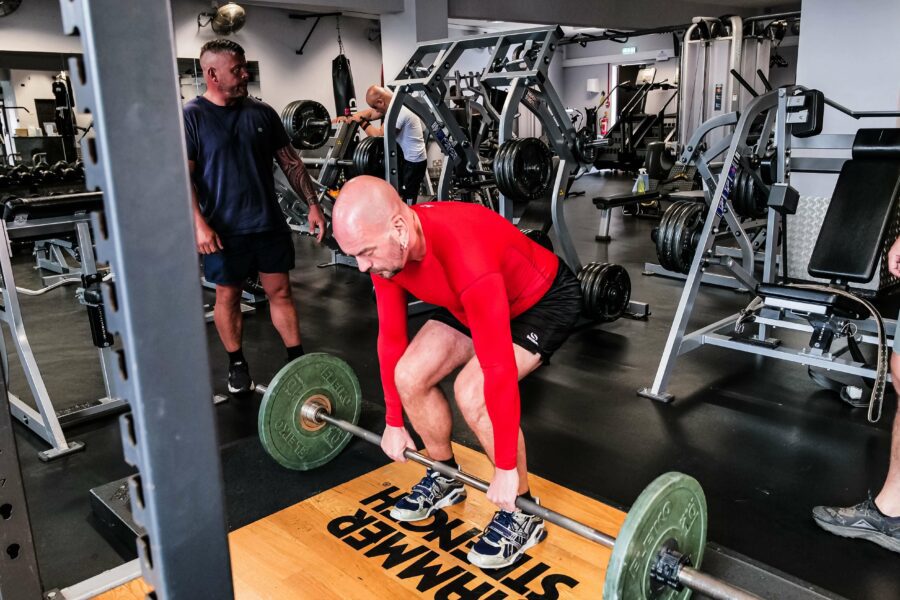 A man lifting a barbell from the floor wearing a red long sleeve shirt