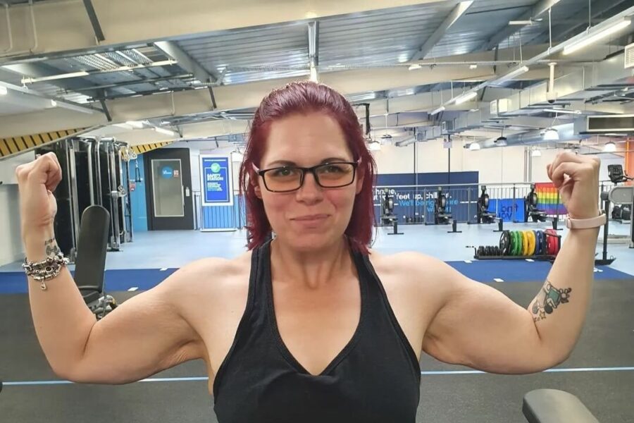 A woman in glasses and a vest flexing her arms, facing the camera