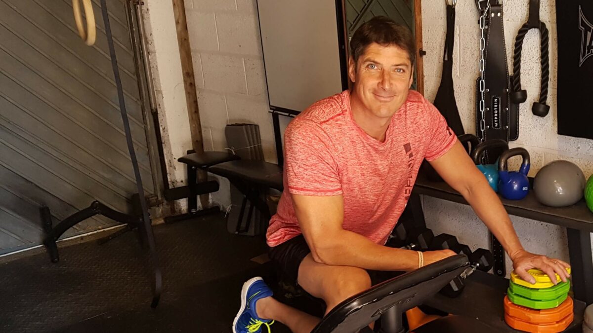 A man wearing a pink t-shirt kneeling by some plate weights