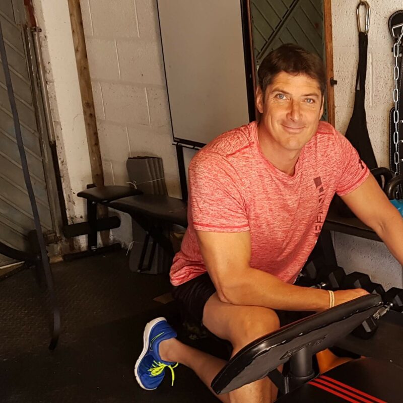 A man wearing a pink t-shirt kneeling by some plate weights