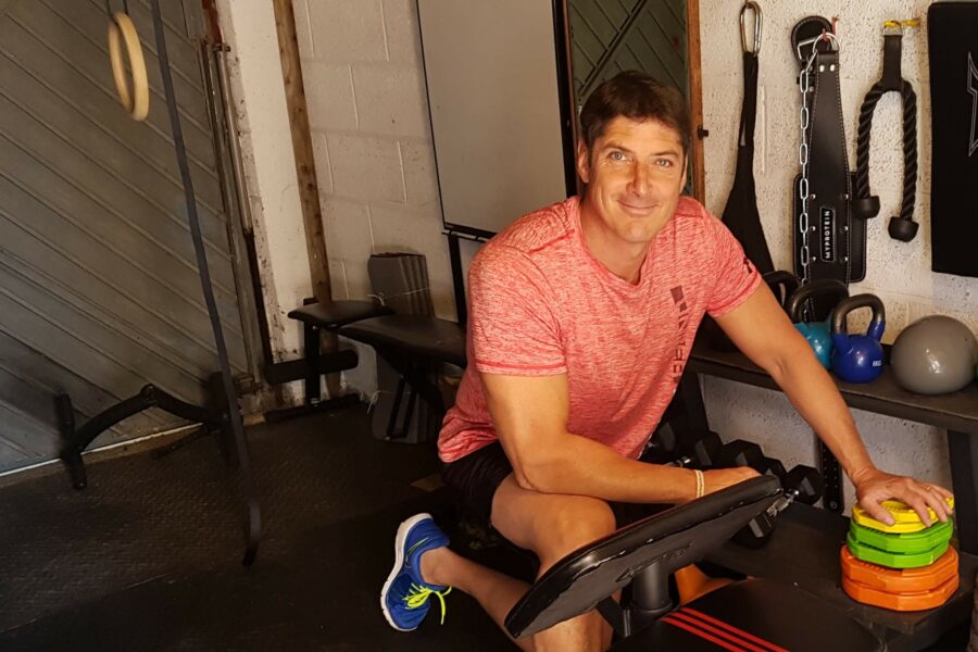 A man wearing a pink t-shirt kneeling by some plate weights